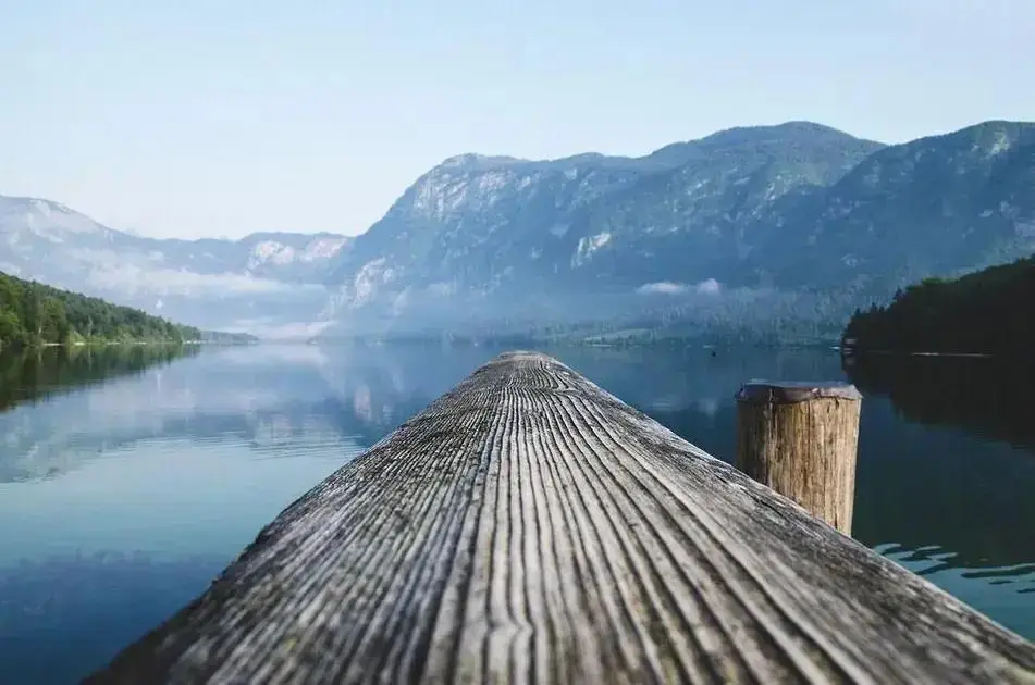 autocuidado para reduzir estresse e ansiedade: pier de madeira sobre lago calmo com montanhas ao fundo simbolizando silêncio mental e tranquilidade