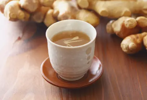 Xícara de chá de gengibre com raízes de gengibre ao fundo em ambiente terapêutico