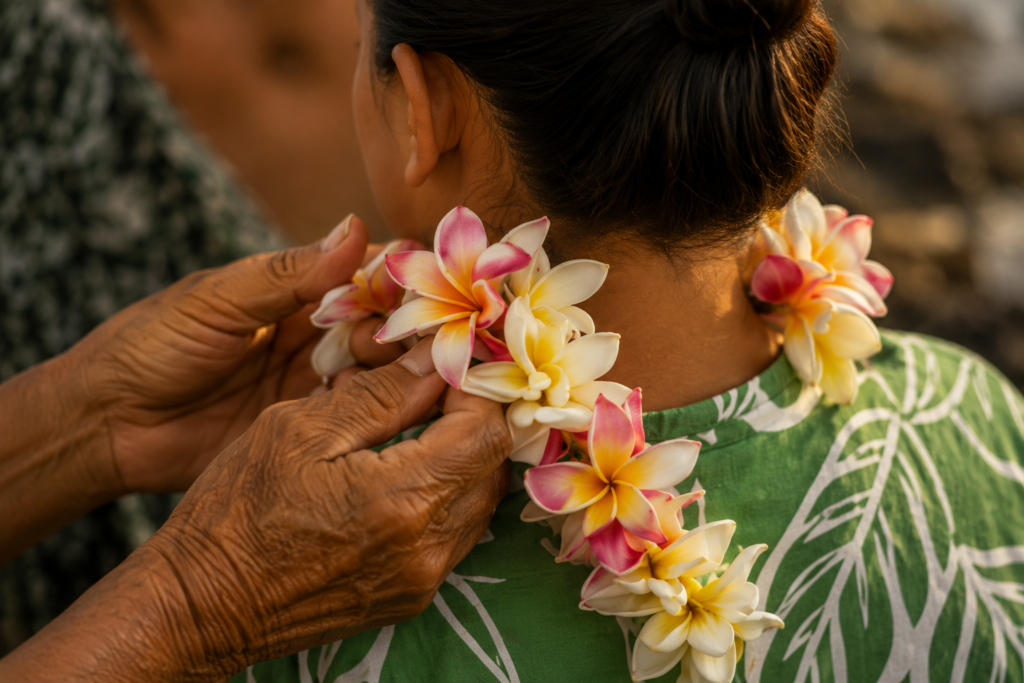 Mãos colocando cuidadosamente um colar de flores no pescoço de outra pessoa durante uma cerimônia havaiana.